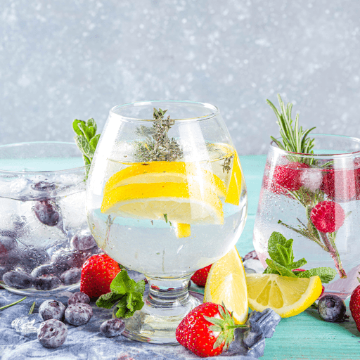 Sparkling drink with lemon slices, berries, and herbs in stem glass