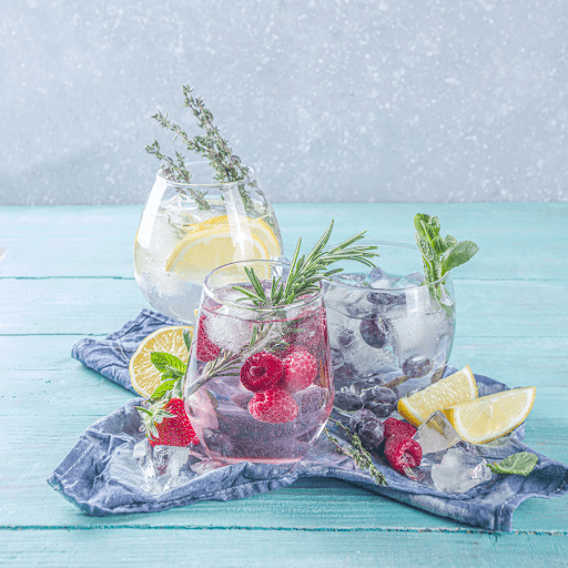 Three berry gin and tonic cocktails with lemon, mint, and rosemary